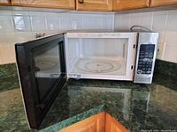 Microwave door open showing interior with glass turntable inside on green countertop and white tiled wall.