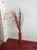 Tall reddish-brown wood grain finish vase with an artificial fountain grass arrangement including green and reddish-brown grasses and small leaf accents.