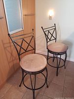 Two upholstered microfiber bar counter stools with metal frames, round beige cushioned seats, and rotating seats. Shown from front angle.