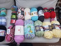 Multiple brand new yarn skeins in assorted colors and types displayed on a couch.