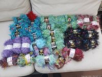 Overview photo showing multiple skeins of brand new eyelash and novelty yarns in various bright colors scattered on white couch.