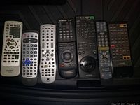 Photo showing seven assorted remote controls from various brands on a black surface.