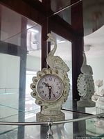 Front view of the vintage peacock clock showing the clock face embedded in the body and the ornate feather design.