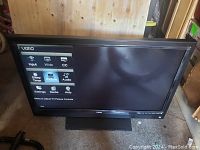 Front angled view of VIZIO 42" LCD TV turned on showing settings menu on screen, black bezel and built-in wide rectangular stand base.