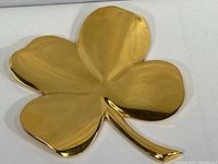 Top and angled view of the shiny 24k gold plated four leaf clover, showing smooth reflective surface and leaf shapes.