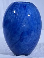 Front side of sky blue art glass vase with marbled smoky white swirls on a plain surface.