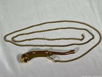 Full view of the boatswain's whistle with brass chain laid out on fabric, showing the length and condition of chain.