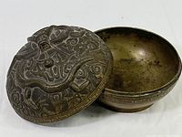 Overall view of the brass covered bowl with lid removed showing the interior and exterior of the bowl and lid with serpent motif.