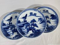 Set of three vintage blue and white porcelain plates showing detailed water landscape and architectural scenes in blue on white base.
