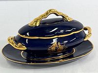 Oval covered trinket dish in cobalt blue with gold detailing and classical scene on side, shown with lid on