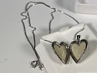 Photo showing the heart-shaped locket open, revealing photo compartments inside, and the attached sterling silver chain.