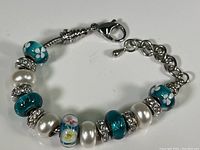 Full view of the silver tone charm bracelet displaying various glass flower beads, faux pearl beads, and crystal spacers with lobster clasp.