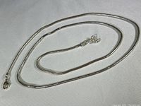 Full view of the long silver chain necklace laid out on a flat light grey surface showing lobster clasp and chain design details.