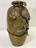 Front and side views of vintage solid brass vase decorated with raised vine and leaf motifs, showing natural patina and aged condition.