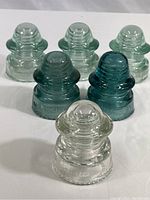 Six glass electrical insulators in three models, clear Hemingray in front, green McLaughlin in back rows