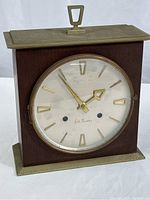 Full front view of the clock showing wood case with metal elements and clock face.