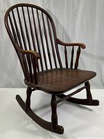 Front-side view of the vintage wooden rocking chair, showing the curved spindle backrest, armrests, seat, and rocking base.