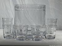 Wide shot showing large crystal ice/champagne bucket with six glasses arranged in front (2 highball, 4 old fashioned). Clear crystal with rectangular cut design near edges.