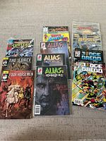 Set of 12 comic books laid out on carpet, showing variety of titles and cover art.