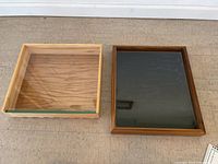Two wooden square display pieces side by side on a concrete surface, one light wood and one dark wood with black base.