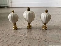 Three white porcelain Lenox finials with brass fittings arranged side by side on floor, showing front and side profiles.