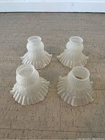Four frosted white glass lamp shades with ribbed texture and ruffled edges, arranged upright to show overall shape and design.