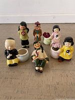 All six Japanese figurines arranged on floor, alongside their respective small ceramic planters