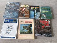 Top view of all seven vintage fishing books laid out on a surface, showing their covers and titles.