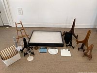 View of all items arranged on floor: black display case with glass top, multiple wooden and metal display stands of varying sizes, and a white box holding striped cardboard items.