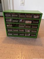 Green metal garage organizer filled with various small household and garage parts in transparent drawers.