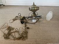 Shows the hangable light fixture lying horizontally with attached hanging chain and separate frosted glass shade on a carpeted floor.