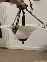 Light fixture held up showing frosted ribbed glass shade suspended by decorative bronze-tone chains and metal supports.