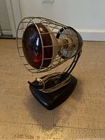 Side angled view of the heat lamp showing the red bulb inside the protective metal cage, black base, and wrapped power cord.