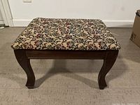 Front view of a heated electric foot stool with floral fabric upholstery and wooden legs.