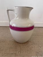 Front view of the large off-white ironstone pitcher with a bright pink band and angular handle.