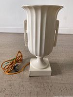 Front view of white ceramic urn-shaped Lenox lamp on square pedestal with yellow fabric electrical cord