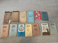 Overhead photo of 13 vintage railroad time books arranged in two rows on a concrete floor to show variety and condition
