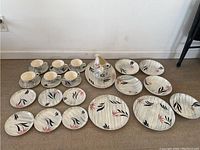 Full set of Stetson dinnerware arranged on floor showing cups, saucers, plates, bowls, sugar bowl, gravy boat, and serving plate with distinct abstract pink and black leaf patterns on off-white background.