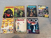 All seven comic and magazine books in the lot laid out on floor, showing front covers and condition.