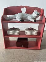 Front view of the red wooden 3-tier shelf with ceramic cat on top shelf, two flower boxes on middle shelf, and trinket box on bottom shelf