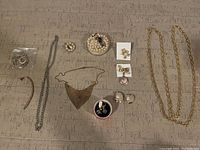 Overview of entire jewelry lot on flat surface showing necklaces, earrings, brooches, and pins arranged for display.