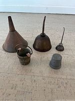Overview of all five vintage garage items on floor: tin funnel, two oilers, mixing cup, bucket ashtray