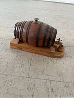 Wooden barrel cigarette dispenser viewed from above and one side, showing metal bands and wooden tap.