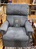 Front view of blue upholstered rocker recliner showing padded backrest, seat and armrests. Chair is positioned upright with recliner footrest closed.