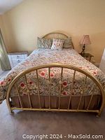 Full view of the brass bed frame assembled with headboard, footboard, and rails in a bedroom setting, showing the curved design and brass finish.