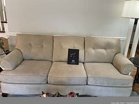 Front full view of the creamy taupe upholstered couch showing tufted cushions and wooden legs