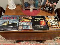 Four coffee table books displayed side by side on a wooden table, titled Titanic, Great Disasters, Mysteries of the Unexplained, and Darkest Hours.