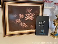 Framed floral still life print featuring pink flowers on a dark brown background, with a label showing lot number 22.