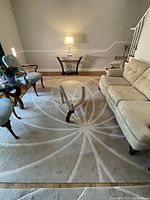 Large cream-colored wool rug with starburst pattern placed in living room under glass-top coffee table, showing full design and condition.