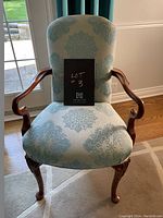 Front view of the wood framed occasional chair showing blue damask floral upholstery and curved wooden arms.